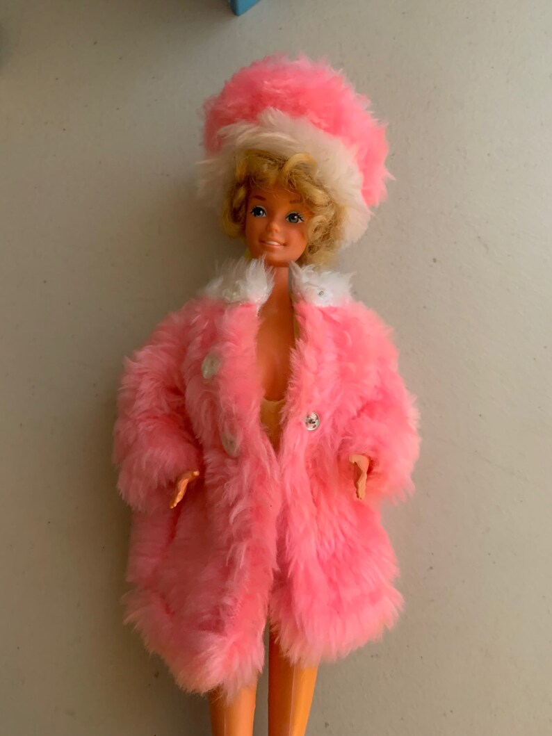 May include: A vintage Barbie doll wearing a pink fur coat and a white and pink fur hat. The doll has blonde hair and blue eyes.