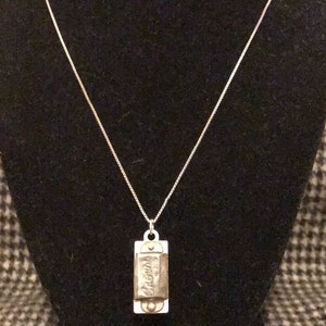 May include: A silver chain necklace with a harmonica pendant. The harmonica is engraved with the word "Hohner".