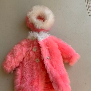 May include: A pink faux fur coat with white trim and three white buttons. The coat has a matching white faux fur hat.