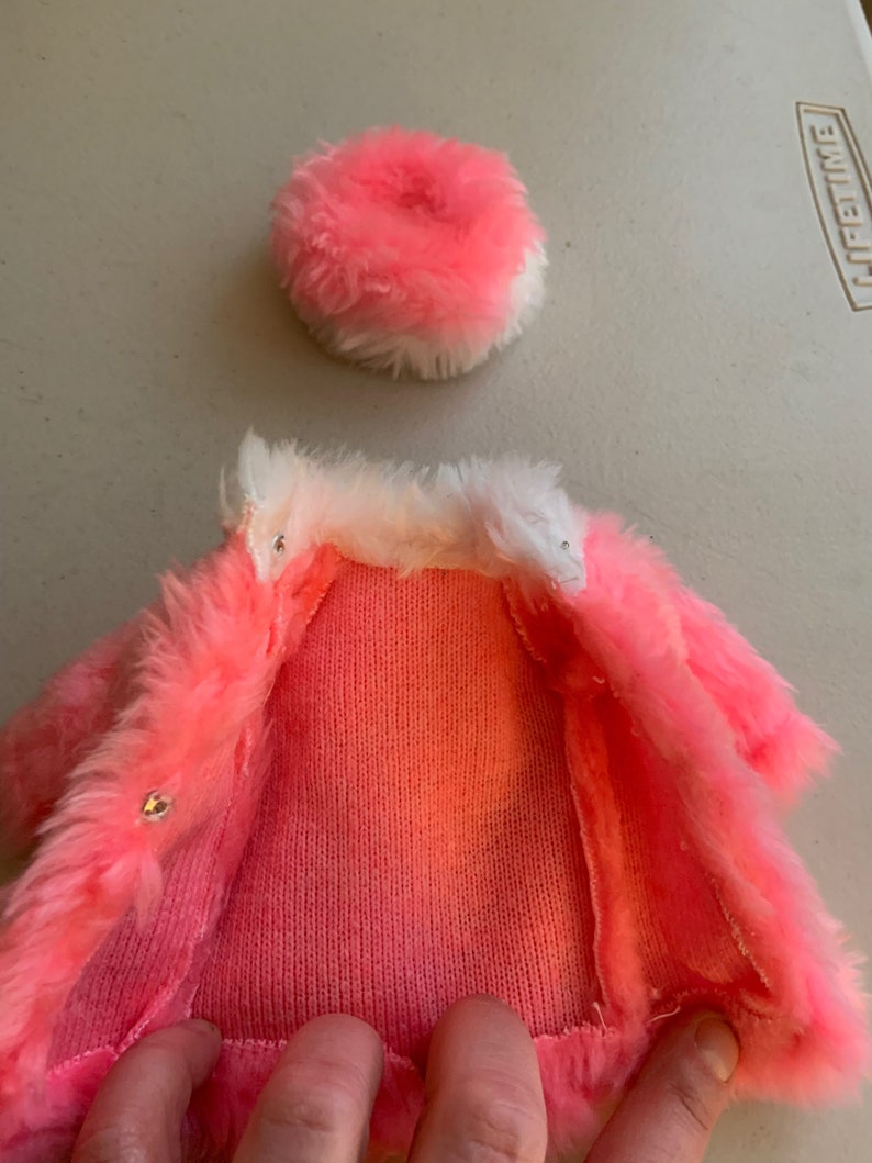 May include: A pink faux fur coat with a white faux fur collar and a matching pink faux fur hat.