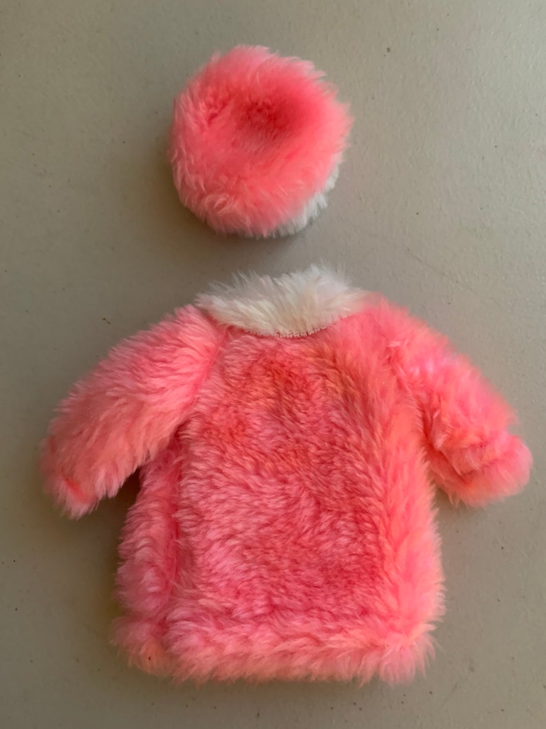 May include: A pink faux fur coat with a white faux fur collar and a matching pink faux fur hat.