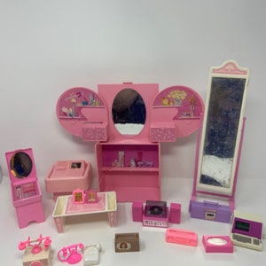 May include: A pink Barbie vanity set with a mirror, a dresser, a table, a phone, a radio, and a record player. The set is made of plastic and has a vintage look.