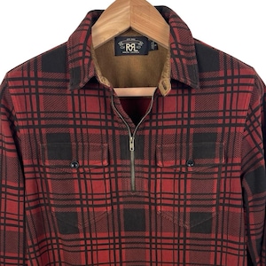 May include: Red and black plaid long-sleeve shirt with a zip-up collar. The shirt has two chest pockets and a brown corduroy collar. The shirt is hanging on a wooden hanger.