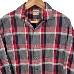 Pode incluir: Uma camisa xadrez de manga comprida em vermelho, branco e azul marinho, pendurada em um cabide de madeira. A camisa apresenta uma frente abotoada e uma gola. A etiqueta diz "McGregor".