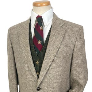May include: A tan tweed blazer with a white collared shirt, green vest, and patterned tie. The blazer has a two-button closure and front pockets. The tie features a red and green stripe design.