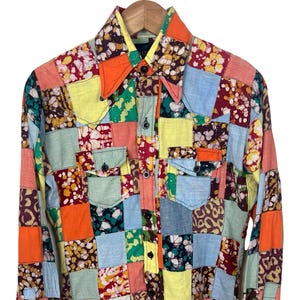 May include: A long-sleeve button-down shirt featuring a multi-colored patchwork design. The garment is composed of various square fabric panels in shades of orange, yellow, light blue, green, and deep red, with some sections displaying floral and animal print patterns.