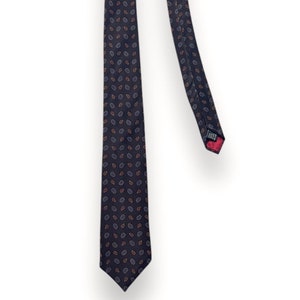 Puede incluir: Una corbata azul oscuro con un diseño de pequeñas hojas repetidas en tonos azules y naranjas.