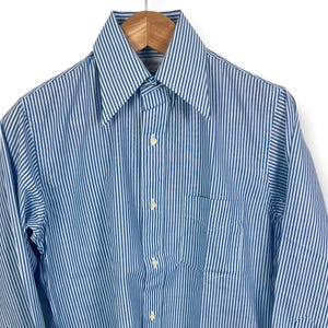 May include: A blue and white striped button-down shirt with a pointed collar and a chest pocket. The long-sleeved shirt is hanging on a wooden hanger. The shirt has white buttons and cuffs.