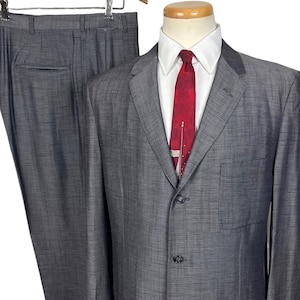 May include: A gray suit with a matching jacket and pants. The jacket has a notched lapel, two front pockets, and a three-button closure. A red tie with a white shirt is visible. The suit is displayed on a mannequin.