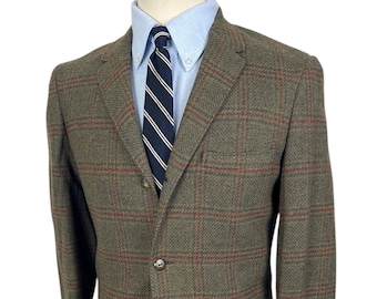 May include: A green and brown checked blazer with red detailing, paired with a light blue shirt and a navy tie with white stripes. The jacket has two front pockets and a three-button fastening.