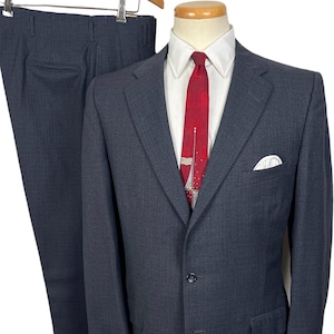 May include: A charcoal gray suit displayed on a mannequin. The suit includes a two-button blazer with a white pocket square and matching trousers. A white dress shirt and a red tie with a sailboat design complete the ensemble. The trousers are hanging on a wooden hanger.