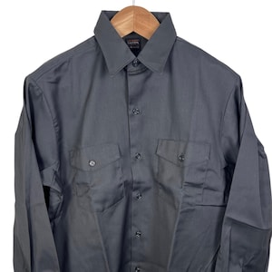 May include: A charcoal gray button-down shirt with two chest pockets and long sleeves. The shirt is hanging on a wooden hanger against a white background. The shirt has a classic collar and buttoned cuffs.