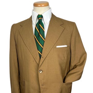 May include: A brown blazer with a single button closure. The blazer has a pocket on the left chest and two pockets on the bottom. The blazer is on a mannequin wearing a white shirt and a green and yellow striped tie.