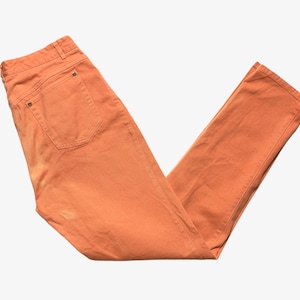 May include: A pair of orange colored jeans. The jeans are folded in half and laid flat on a white background.