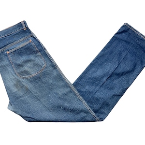 May include: A pair of blue denim jeans folded in a V-shape. The jeans have a back pocket with a stitched flap.
