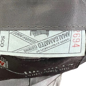 May include: A white tag with black text that reads "Issued by authority of " followed by a logo and the text "Mallalieu Limited" and "John Ford & Son" with a red number "2694" on the right side. The tag is attached to a brown fabric with a white tag that reads "SCQ" in black text.