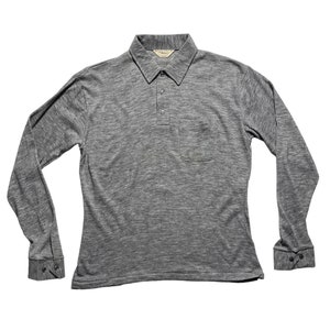 May include: A grey long-sleeved polo shirt with a button-down collar and a single pocket on the left chest. The shirt has a subtle heather pattern.