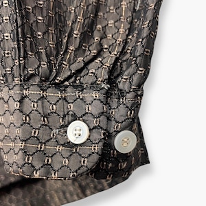 May include: Close-up of a black fabric with a geometric pattern and two white buttons. The fabric has a delicate, see-through quality with a subtle sheen. The buttons are round and have a pearlescent finish.