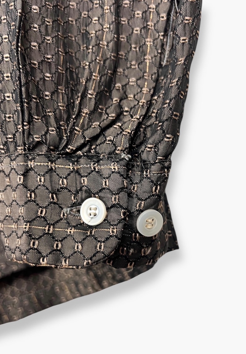 May include: Close-up of a black fabric with a geometric pattern and two white buttons. The fabric has a delicate, see-through quality with a subtle sheen. The buttons are round and have a pearlescent finish.