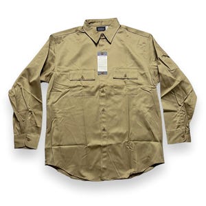 Può includere: Una camicia da lavoro a maniche lunghe di colore kaki con due grandi tasche sul petto e un colletto abbottonato. La camicia ha un'etichetta del marchio sul lato sinistro del colletto.