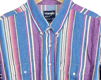 May include: A button-down shirt with vertical stripes in blue, purple, pink, and white. The shirt has two chest pockets and a blue collar. The Wrangler logo is visible on the collar.