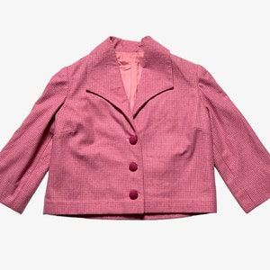 May include: A pink and white checkered blazer with a notched collar and three burgundy buttons. The blazer has a cropped length and three-quarter sleeves.