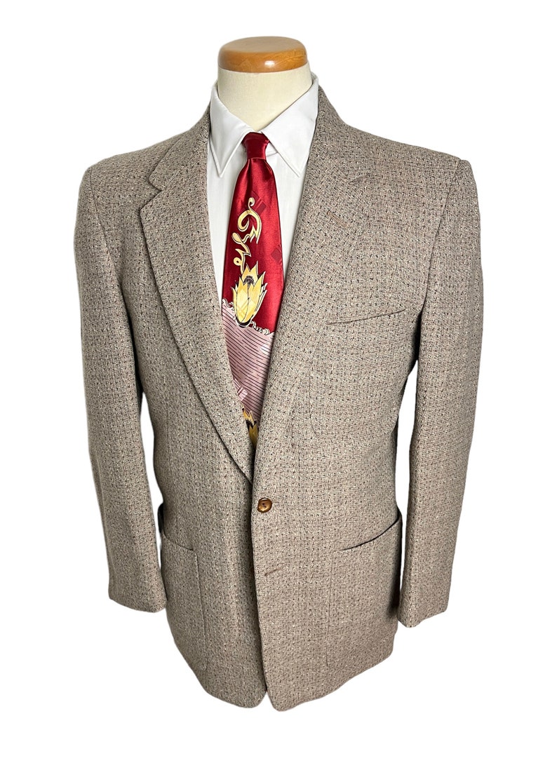 May include: A brown tweed blazer with a single button closure. The blazer has a subtle pattern and two flap pockets.