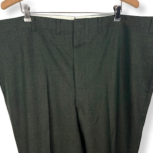 May include: Dark gray dress pants hanging on a wooden hanger. The pants are made of a textured fabric and have a classic, tailored design. The pants are a solid color and appear to be in good condition.