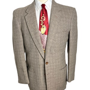 May include: A brown tweed blazer with a single button closure and a patch pocket on the left side. The blazer is on a mannequin wearing a white shirt and a red patterned tie.