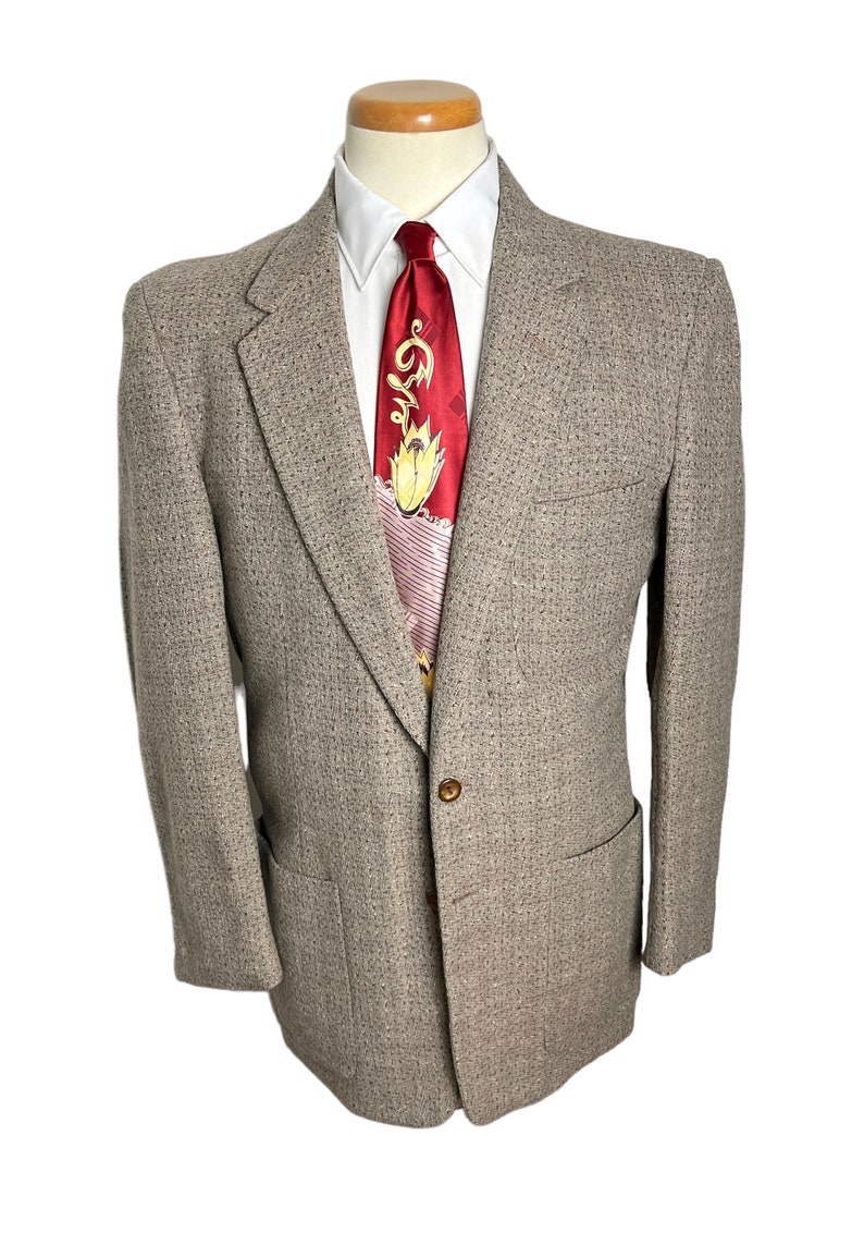 May include: A brown tweed blazer with a single button closure and a patch pocket on the left side. The blazer is on a mannequin wearing a white shirt and a red patterned tie.