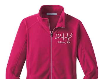 May include: A pink fleece jacket with a zipper closure. The jacket has a white embroidered design of a heart with a stethoscope and a heartbeat line. The text "Allison, RN" is embroidered below the design.