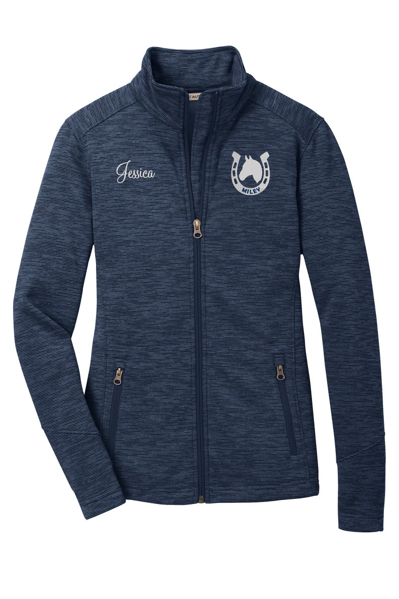 May include: A navy blue zip-up jacket with a white horseshoe and horse head logo that says "MILEY" and the name "Jessica" embroidered on the front.