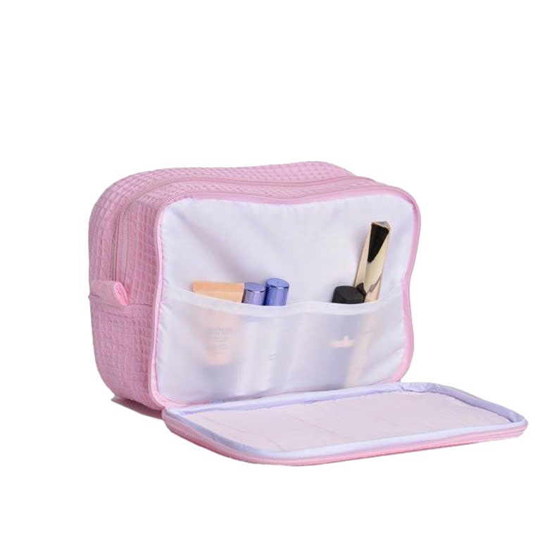May include: A pink quilted makeup bag with multiple compartments and a zipper closure. The bag is open and has several makeup items inside, including a foundation bottle, mascara, and eyeliner.