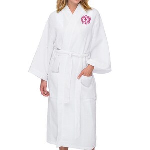 May include: White waffle weave robe with a pink monogram on the chest. The robe has a sash tie and two pockets.