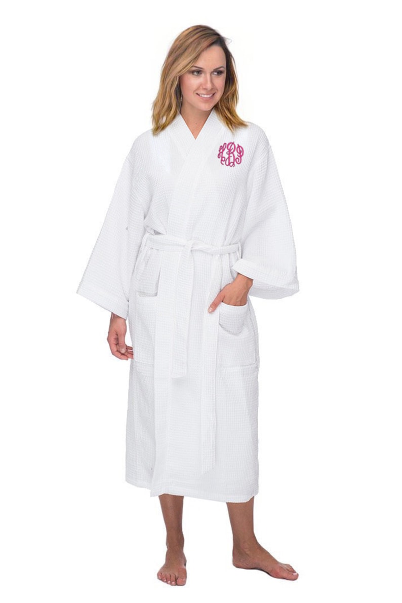 May include: White waffle weave robe with a pink monogram on the chest. The robe has a sash tie and two pockets.