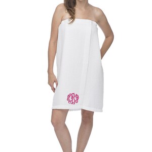 May include: White waffle weave bath wrap with a pink monogram. The wrap is worn by a person standing on a white background.
