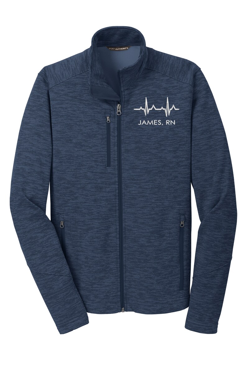 May include: A navy blue fleece jacket with a zipper closure and two zippered pockets. The jacket has a white heartbeat graphic and the text "JAMES, RN" on the front.