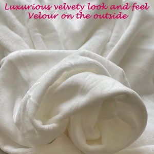 May include: Close-up of a white, soft, velvety fabric. The fabric is folded and bunched up, showing its texture and luxurious feel.