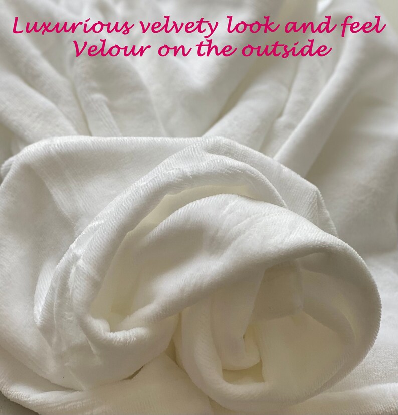 May include: Close-up of a white, soft, velvety fabric. The fabric is folded and bunched up, showing its texture and luxurious feel.