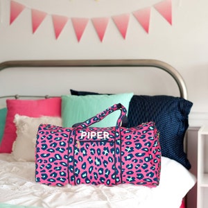 Pu&ograve; includere: Borsa da viaggio rosa con stampa leopardata, cerniera bianca e il nome "PIPER" stampato sul davanti.