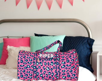 May include: Pink leopard print duffel bag with a white zipper and the name "PIPER" printed on the front.