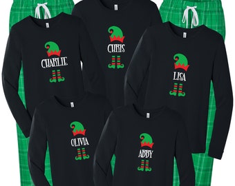 Könnte beinhalten: Fünf schwarze Langarmshirts mit grünen Elfenmützen und den Namen "Charlie", "Chris", "Lisa", "Olivia" und "Abby". Jedes Shirt wird mit grünen karierten Schlafanzug-Hosen kombiniert.