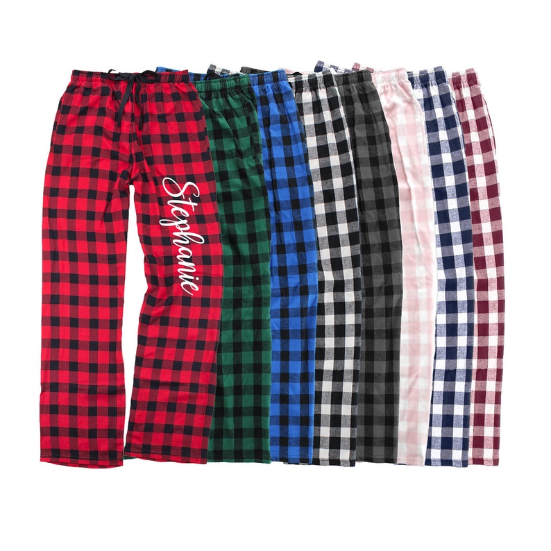 K&ouml;nnte beinhalten: Ein Set aus acht Paar karierten Schlafanzug-Hosen in verschiedenen Farben, darunter Rot, Gr&uuml;n, Blau, Schwarz, Wei&szlig; und Rosa. Die Hosen haben einen personalisierten Namen, "Stephanie", der auf die rote Hose gestickt ist.