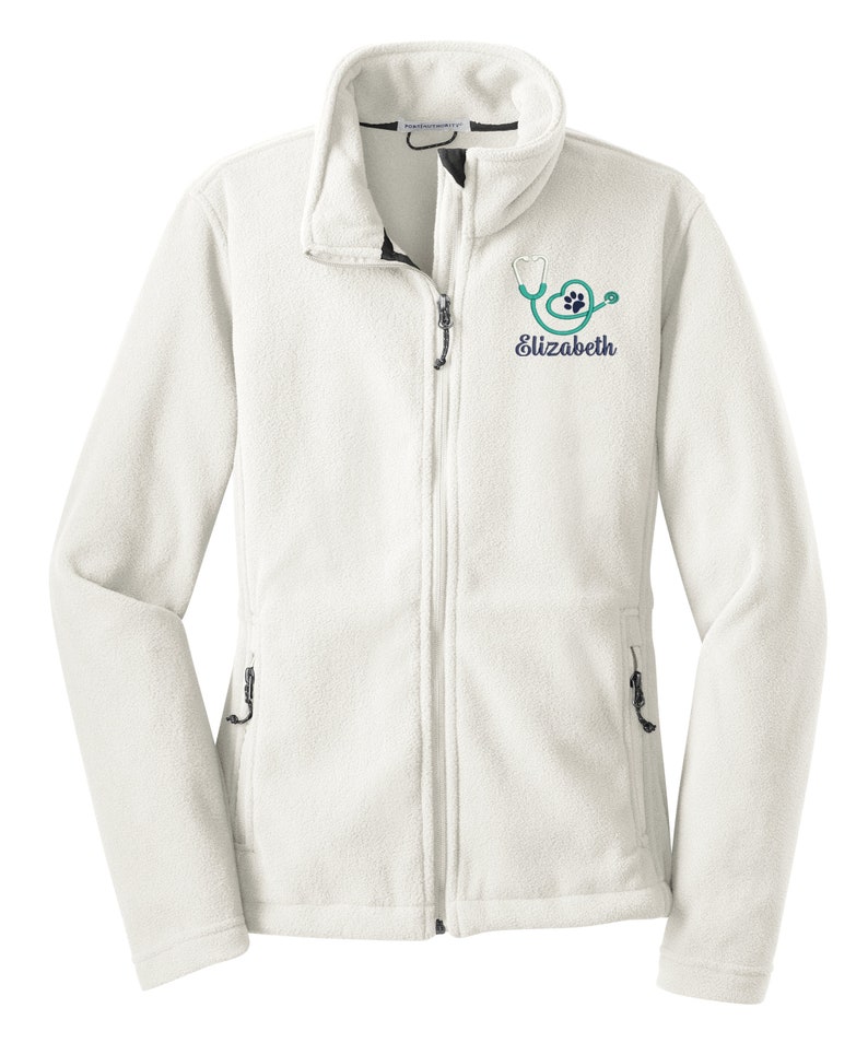 May include: White fleece jacket with a zipper closure and two zippered pockets. The jacket has a stethoscope and paw print logo embroidered on the left chest with the name "Elizabeth" underneath.