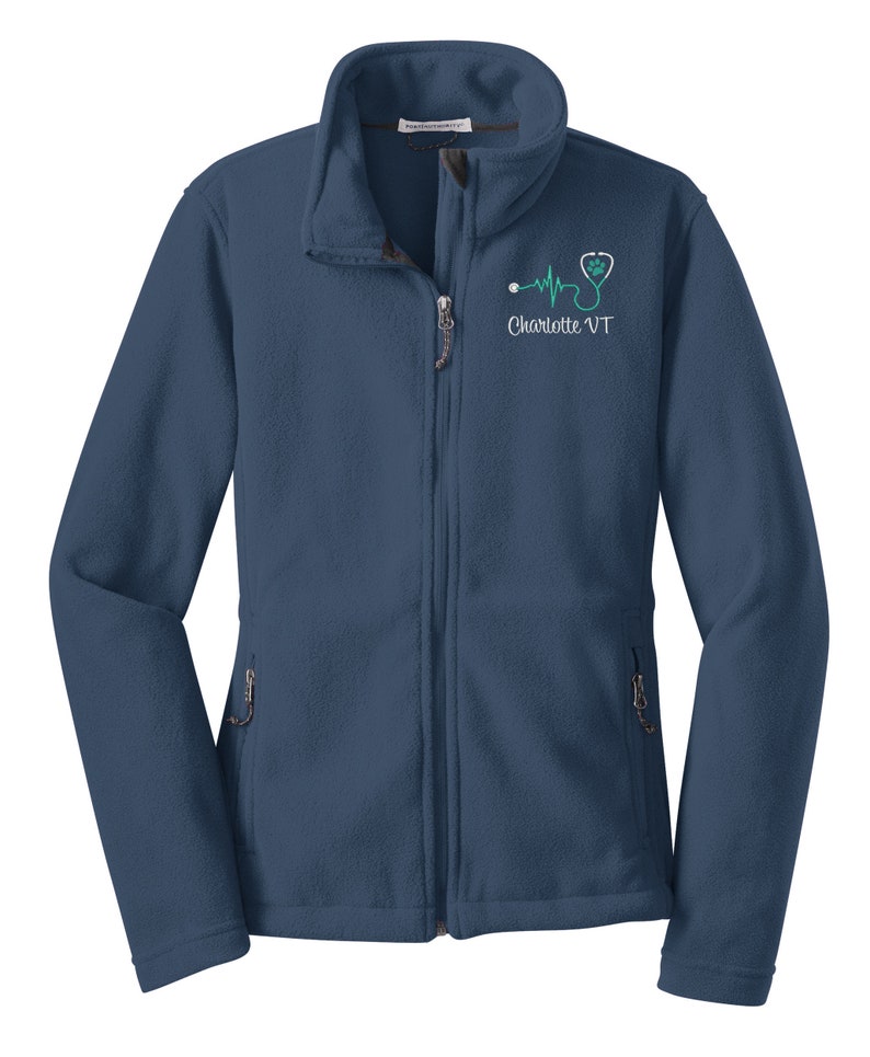 May include: A navy blue fleece jacket with a zipper closure and two pockets. The jacket has an embroidered design on the left chest featuring a stethoscope, a heart, and a heartbeat line with the text "Charlotte VT".