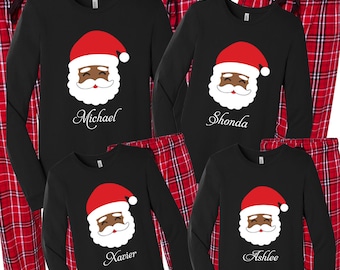 Puede incluir: Pijama negro de manga larga con pantalones de cuadros rojos y negros. Las camisas presentan una imagen de dibujos animados de un Papá Noel negro sonriente con los nombres "Michael", "Shonda", "Xavier" y "Ashlee" impresos debajo.