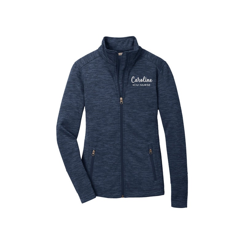 May include: A navy blue zip-up jacket with a heather pattern. The jacket has a white embroidered name "Caroline" and the text "ICU Nurse".