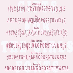 May include: A pink background with five different fonts displayed in pink. The fonts are Annabelle, Sail, Rasta, Izzy Script, Harrington, and Georgia. Each font displays the alphabet in uppercase.