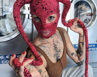 Red mask with long dangling spikes on either side of the head and little black specks print all over.