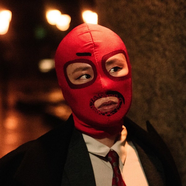 Red lycra mask with squared darker red eye contours and leopard print mouth contour. One side black eyebrow and one side of moustache shape.